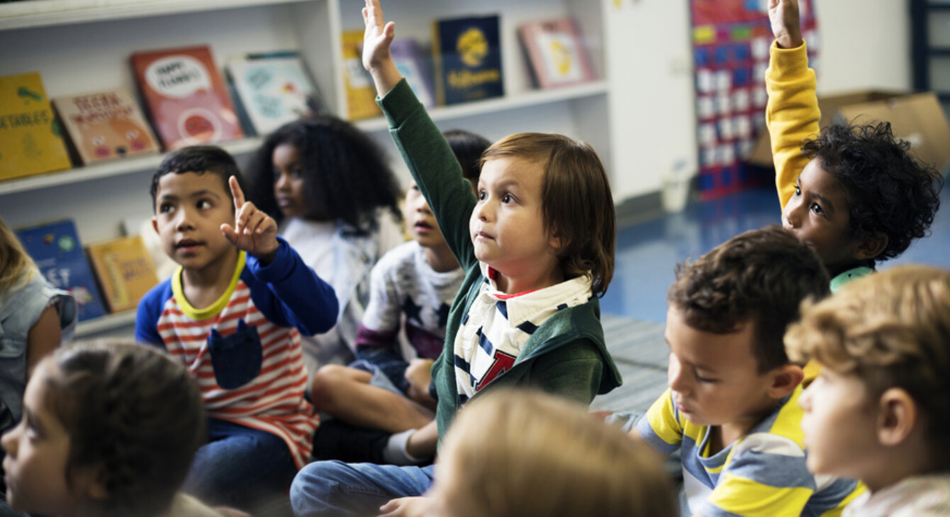 Enfants assis dans une bilbiothèque donc 3 qui lèvent la main